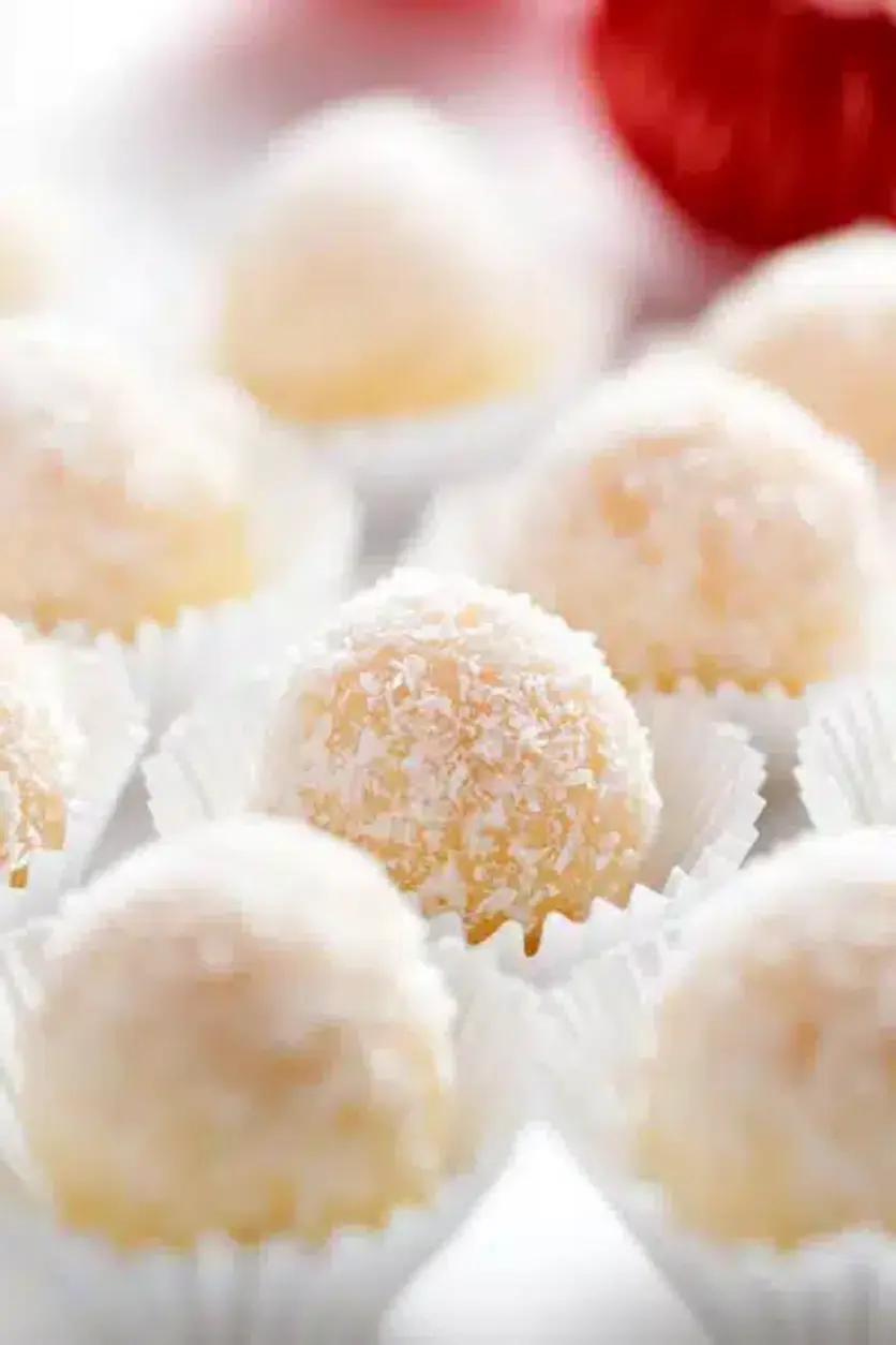 A close-up image of finished snowball coconut fudge truffles on a plate, dusted with coconut shreds, highlighting the final product.